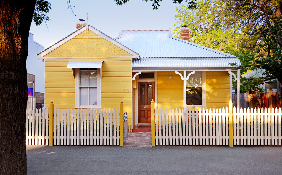 Aménagement d'une façade de maison jaune classique en bois de taille moyenne et de plain-pied avec un toit à deux pans et un toit en métal.