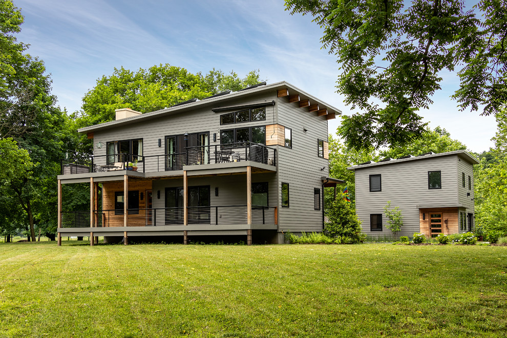 Идея дизайна: двухэтажный, серый частный загородный дом в стиле рустика с комбинированной облицовкой и односкатной крышей