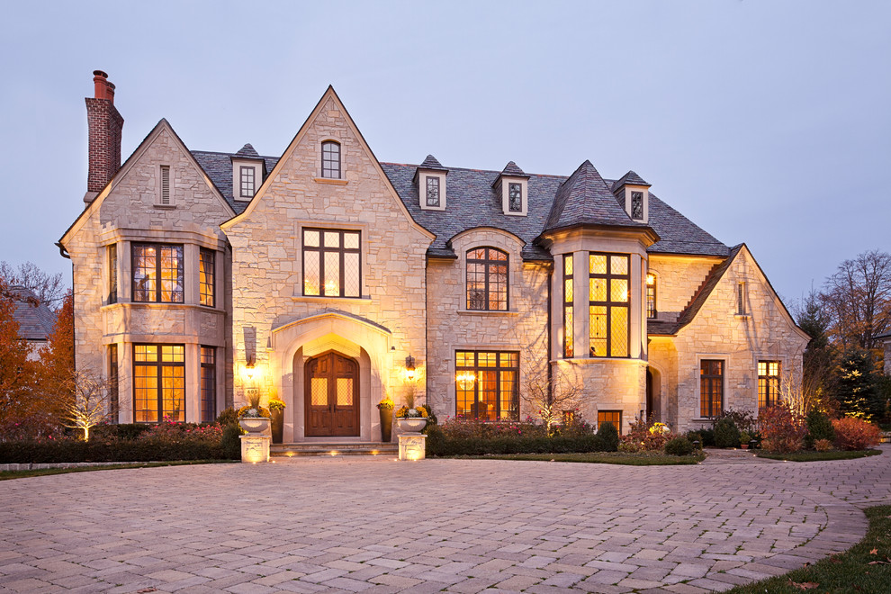 Cette photo montre une façade de maison beige chic en pierre à deux étages et plus avec un toit à quatre pans et un toit en tuile.