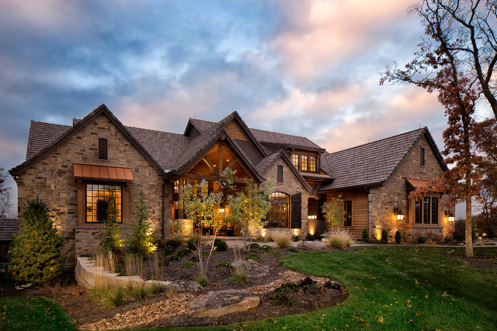 На фото: большой, коричневый дом в стиле рустика с разными уровнями, облицовкой из камня и двускатной крышей с