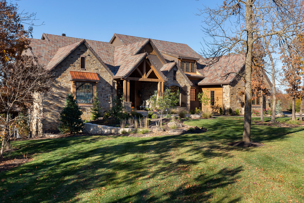 На фото: большой, коричневый дом в стиле рустика с разными уровнями, облицовкой из камня и двускатной крышей с