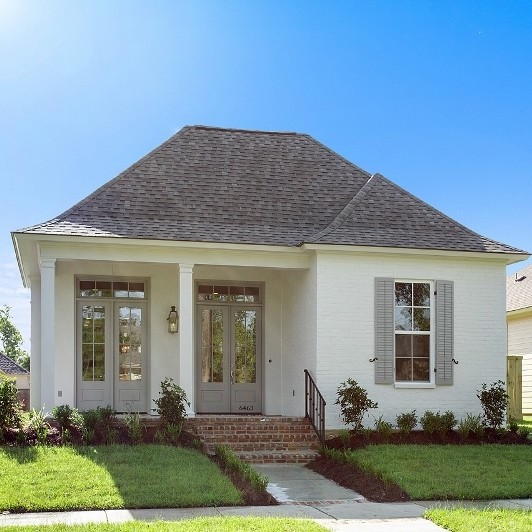 Photo of a medium sized and white modern bungalow brick house exterior in New Orleans with a half-hip roof.