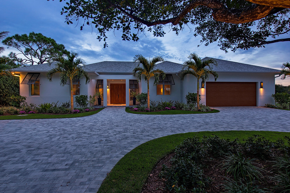 This is an example of a large and white world-inspired bungalow render house exterior in Miami with a hip roof.