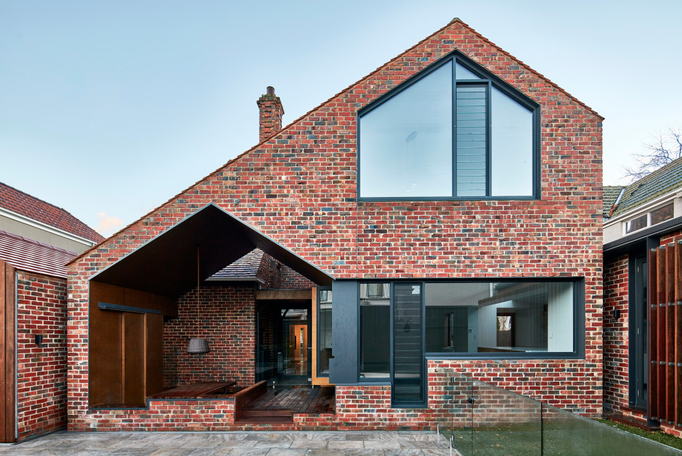 Cette image montre une façade de maison rouge design en brique de taille moyenne et à un étage avec un toit à deux pans.