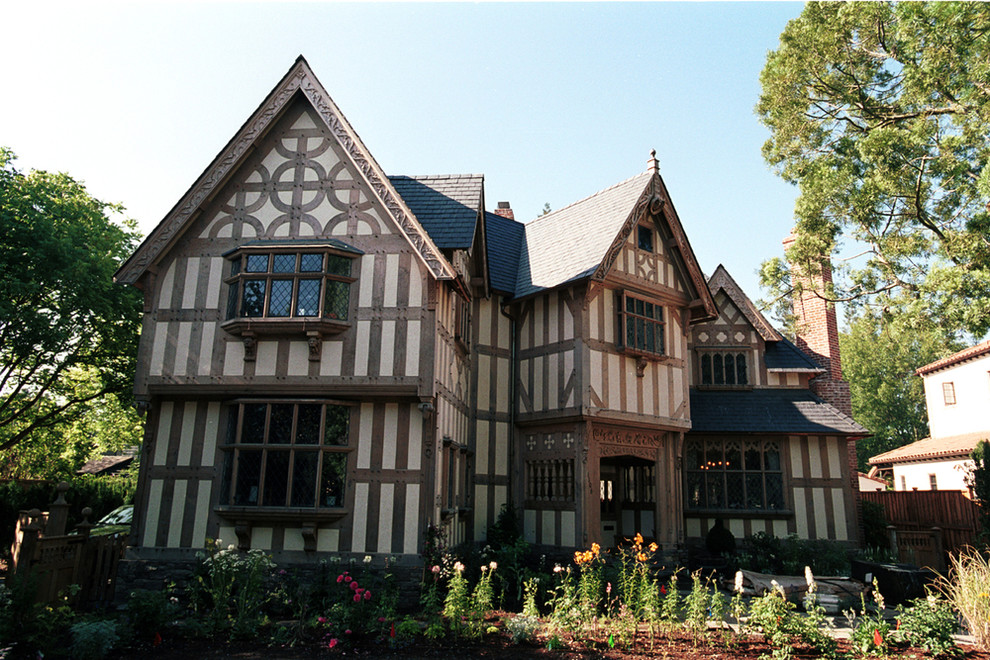 Cette photo montre une grande façade de maison beige chic en stuc à deux étages et plus avec un toit à deux pans et un toit en tuile.