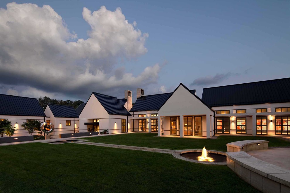 Réalisation d'une très grande façade de maison blanche design en stuc de plain-pied avec un toit à deux pans et un toit en métal.