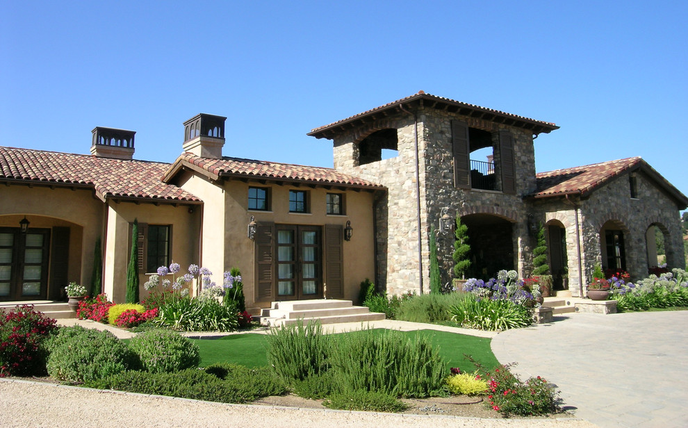 На фото: большой, одноэтажный, разноцветный частный загородный дом в средиземноморском стиле с комбинированной облицовкой, двускатной крышей и черепичной крышей с