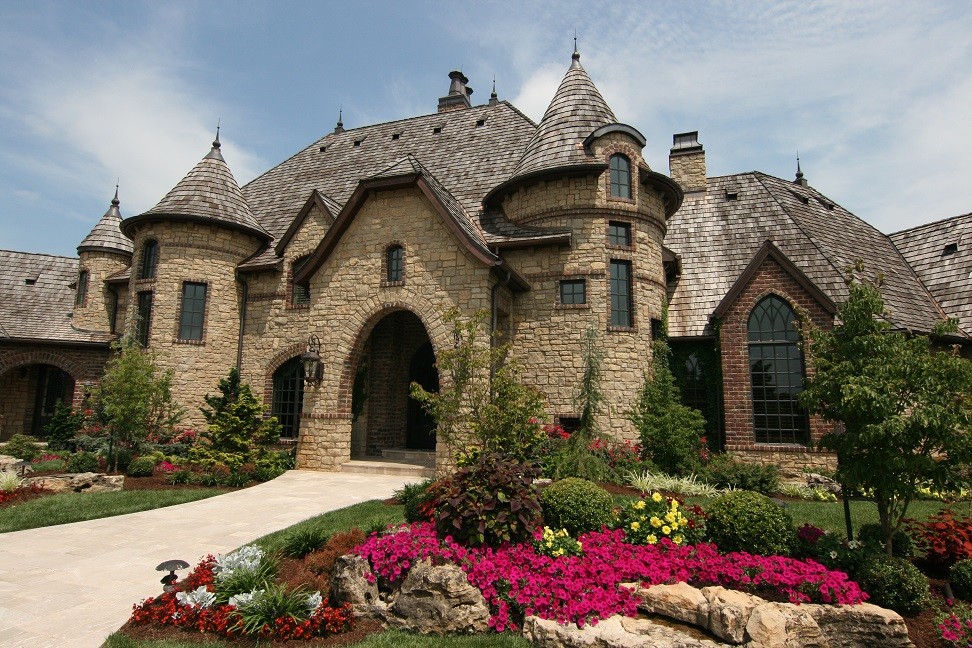 Foto della villa grande marrone mediterranea a due piani con rivestimento in pietra e copertura a scandole