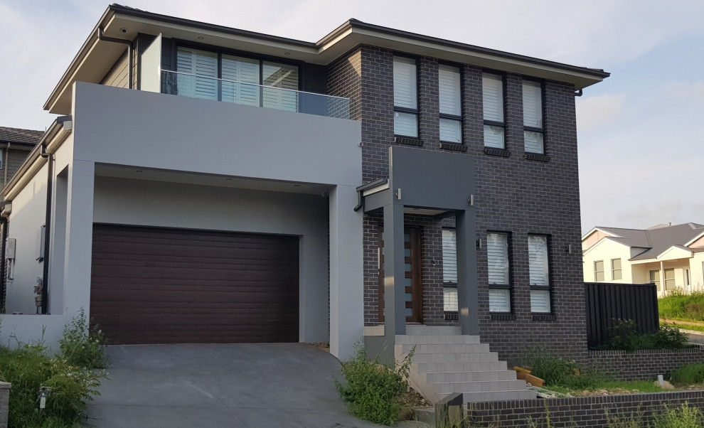 Example of a large minimalist gray two-story brick house exterior design in Sydney with a hip roof and a tile roof