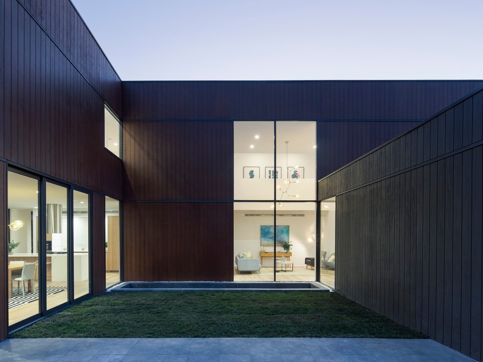 Cette image montre une très grande façade de maison noire design en bois à un étage avec un toit plat.