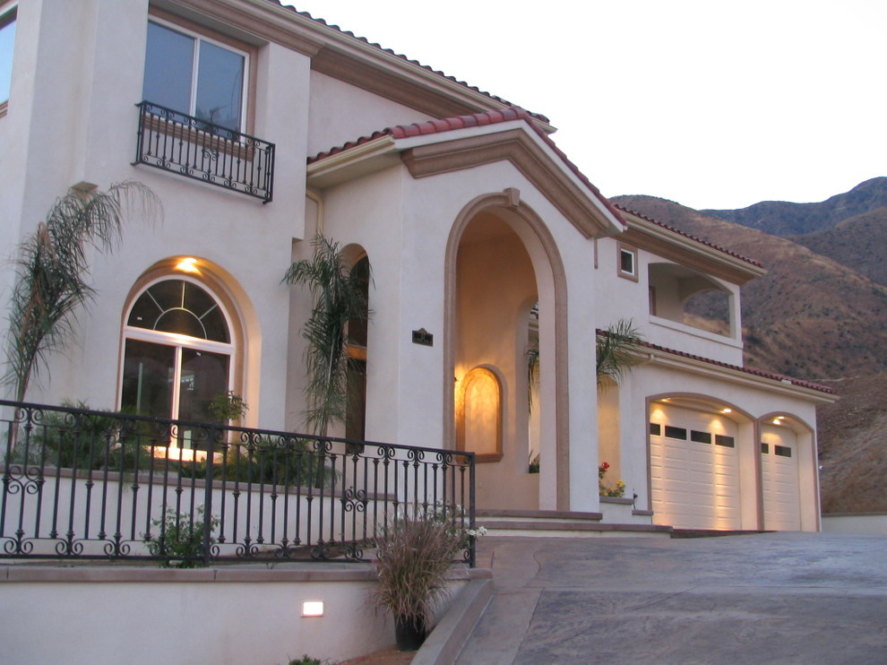 Idée de décoration pour une grande façade de maison beige méditerranéenne en stuc à un étage avec un toit à quatre pans.