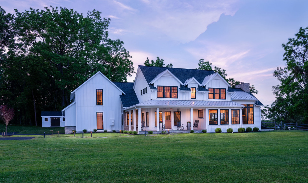 Immagine della villa bianca country a due piani con copertura a scandole, tetto nero e pannelli e listelle di legno