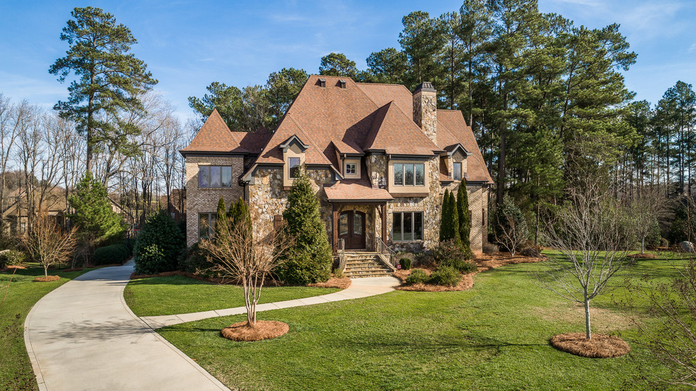 Traditional brown two-story stone house exterior idea in Charlotte with a hip roof and a shingle roof