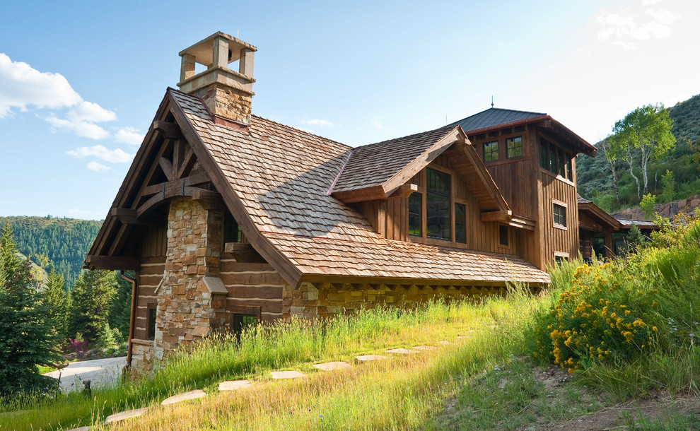 Immagine della facciata di una casa grande marrone rustica a tre piani con rivestimento in legno e tetto a capanna