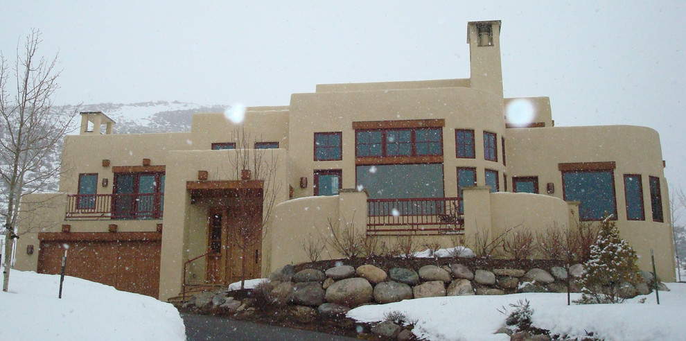 Cette image montre une très grande façade de maison beige sud-ouest américain en stuc à un étage avec un toit plat.