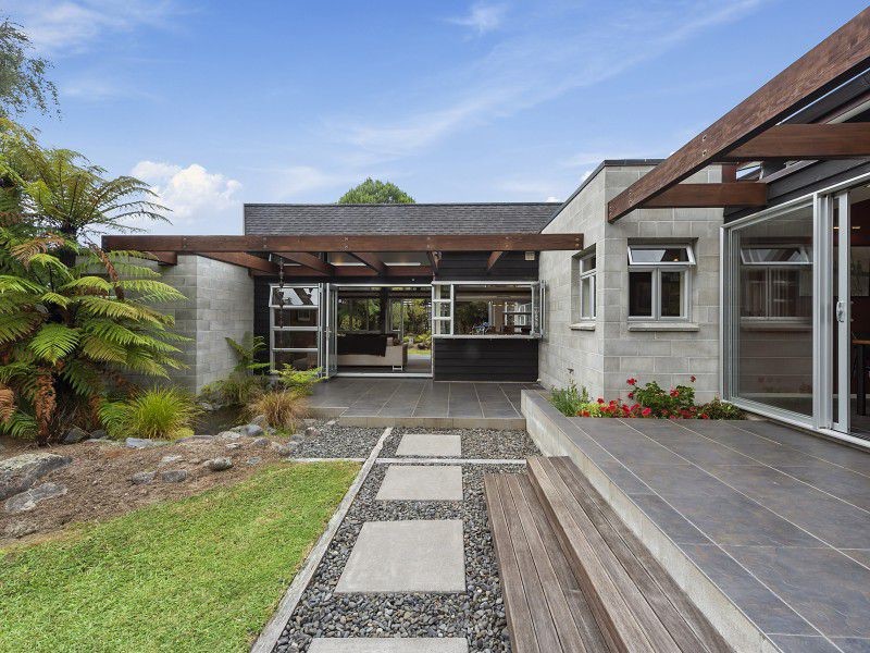 Mittelgroßes, Einstöckiges Mid-Century Einfamilienhaus mit Betonfassade, grauer Fassadenfarbe, Satteldach und Schindeldach in Auckland