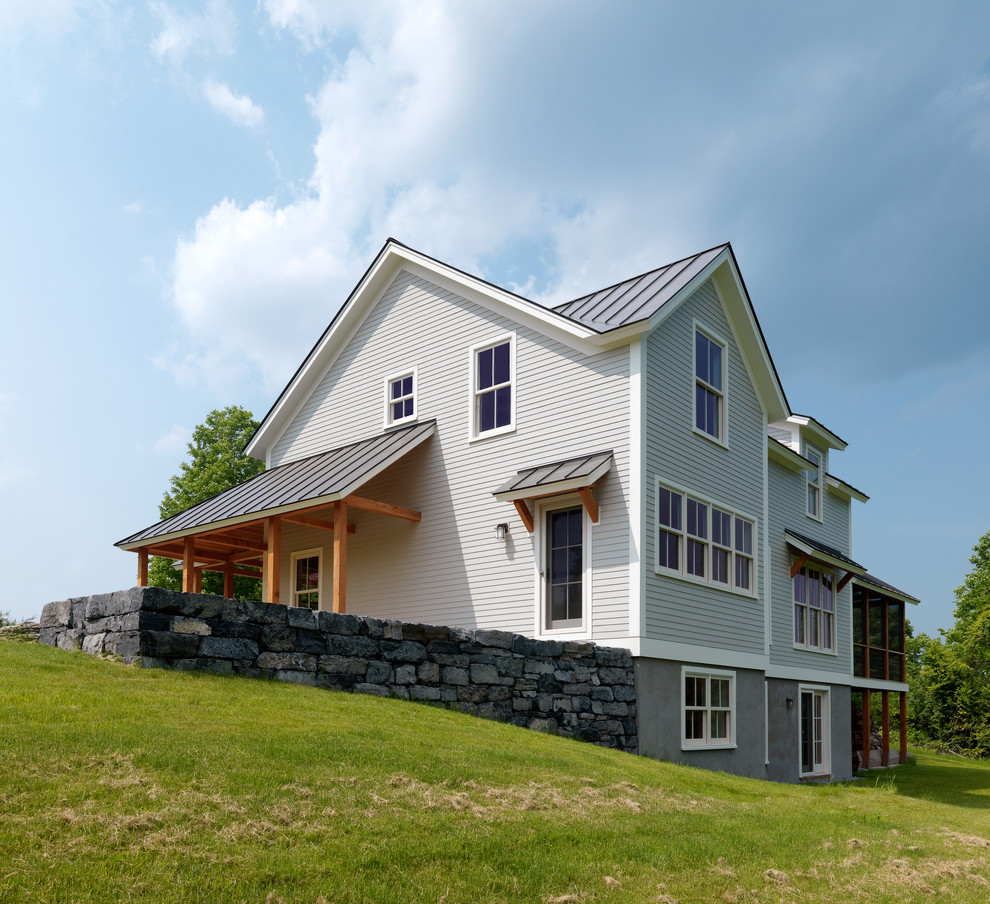 Immagine della facciata di una casa grigia country a tre piani con terreno in pendenza