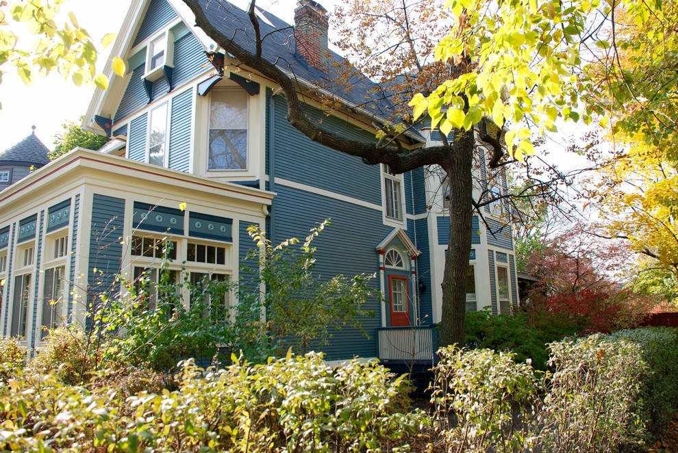 Пример оригинального дизайна: большой, трехэтажный, деревянный, синий частный загородный дом в викторианском стиле с двускатной крышей и крышей из гибкой черепицы