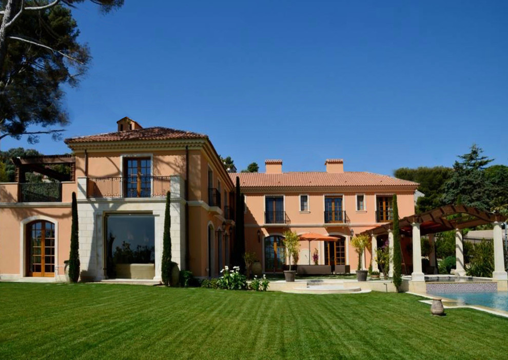 Idée de décoration pour une très grande façade de maison rose méditerranéenne en stuc à deux étages et plus avec un toit à quatre pans et un toit en tuile.