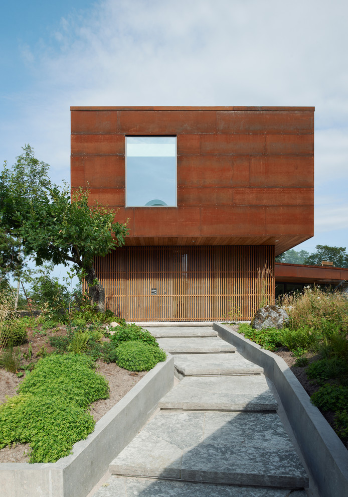 This is an example of a large and brown contemporary two floor house exterior in Stockholm with a flat roof and wood cladding.