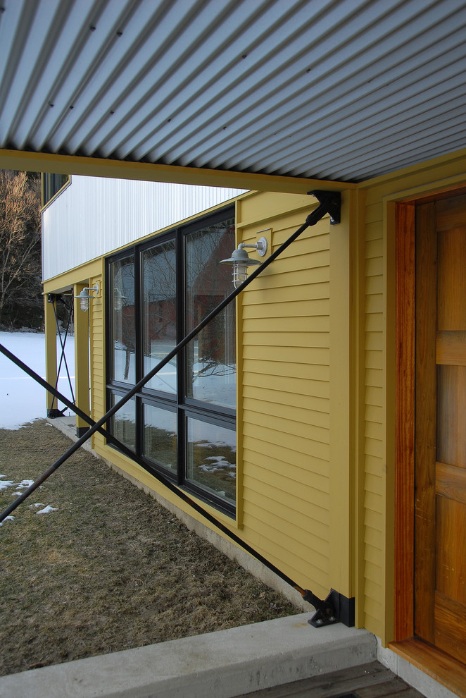Modelo de fachada de casa multicolor campestre grande de dos plantas con revestimientos combinados, tejado de un solo tendido y tejado de metal