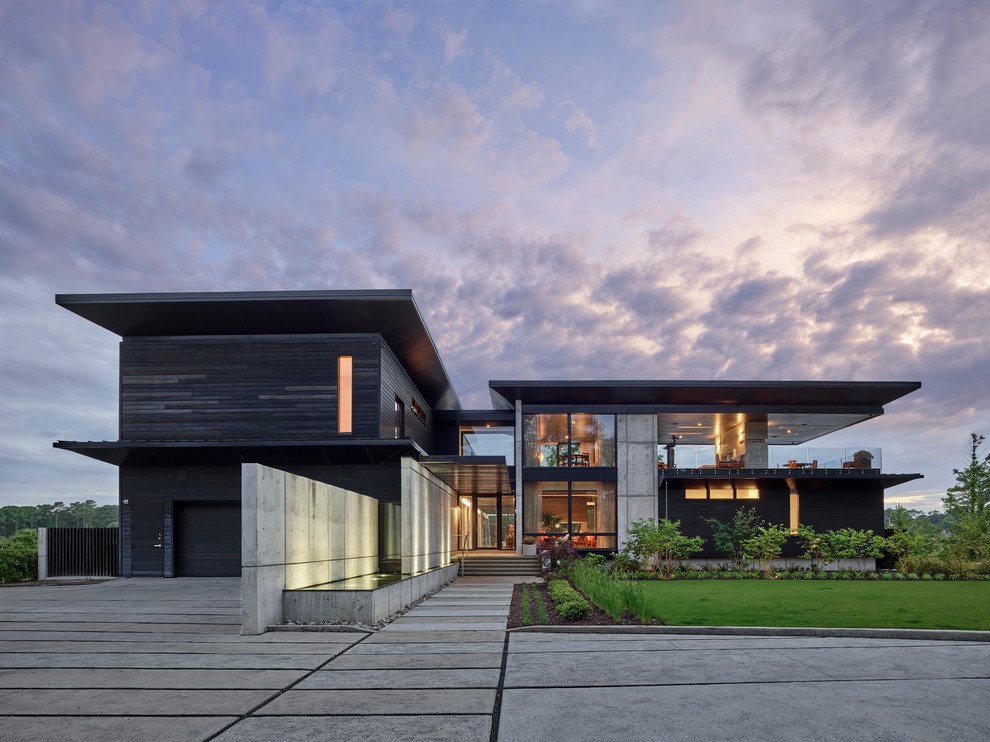 Aménagement d'une grande façade de maison noire moderne à un étage avec un toit plat et un revêtement mixte.
