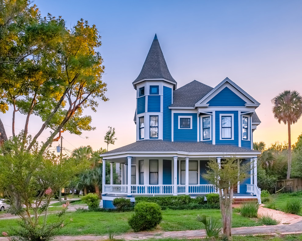 На фото: огромный, деревянный, синий, двухэтажный частный загородный дом в викторианском стиле с крышей из гибкой черепицы и вальмовой крышей с