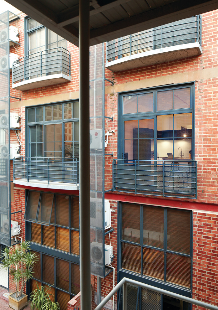 Aménagement d'une façade de maison rouge industrielle en brique à deux étages et plus avec un toit à quatre pans.