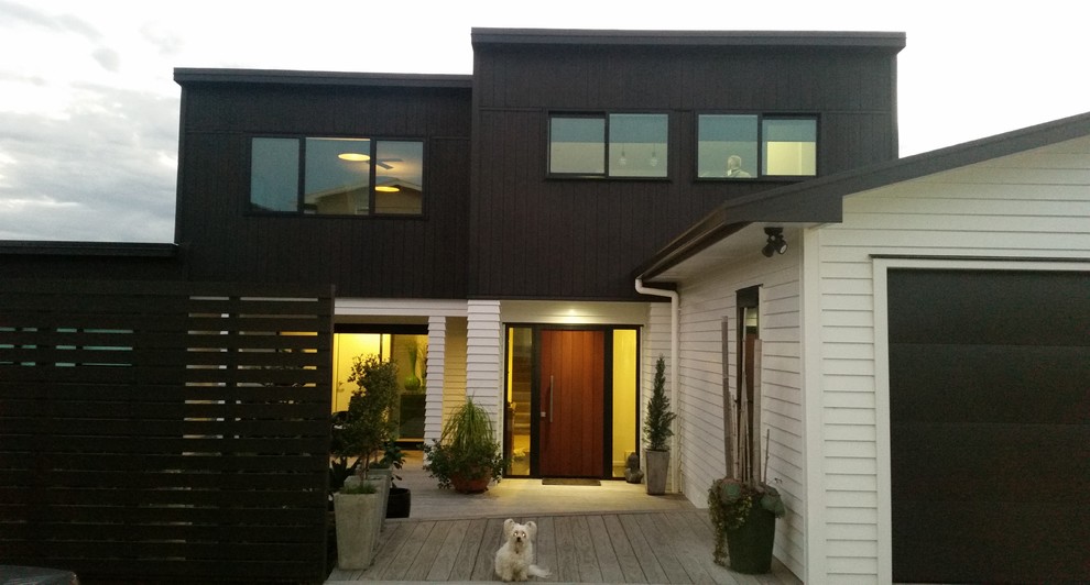 Cette photo montre une façade de maison noire moderne en bois de taille moyenne et à un étage avec un toit plat et un toit en métal.