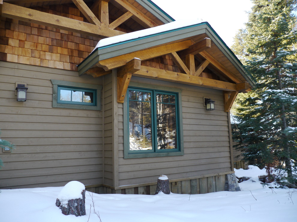 Cette image montre une façade de maison beige chalet en bois de taille moyenne et de plain-pied avec un toit à deux pans et un toit en shingle.
