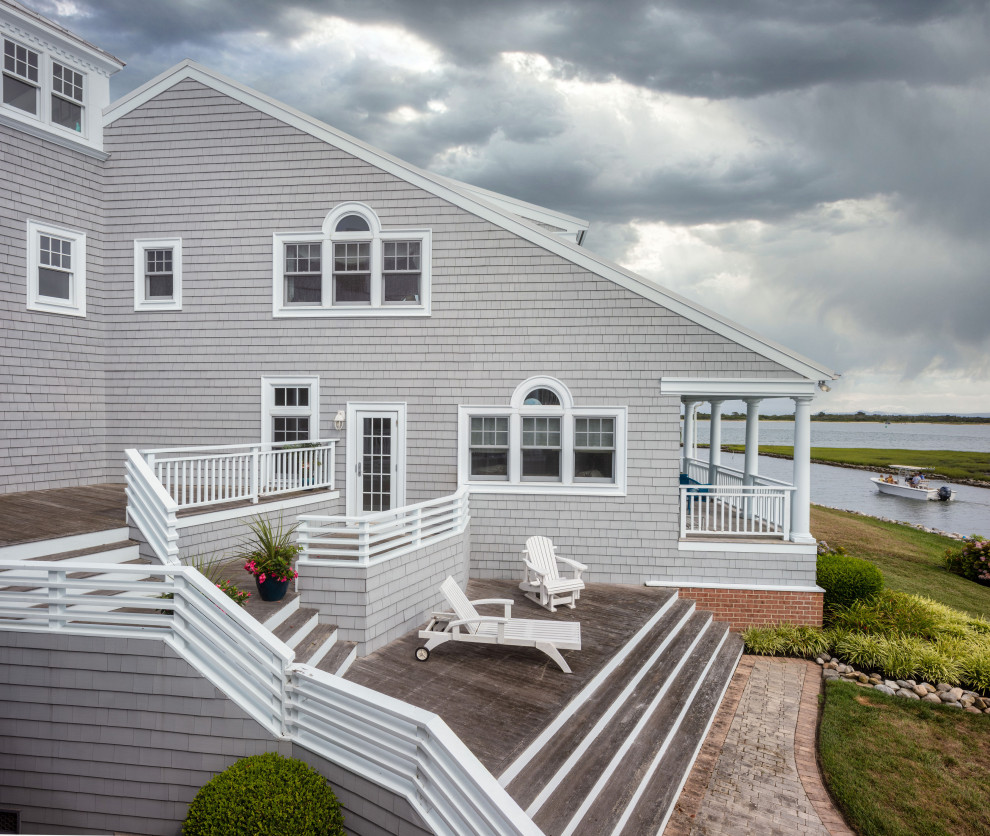 Diseño de fachada de casa beige costera grande de tres plantas con revestimiento de madera, tejado a dos aguas y tejado de metal