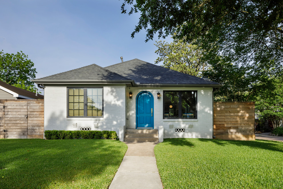 This is an example of a white farmhouse bungalow brick detached house in Houston with a hip roof and a shingle roof.