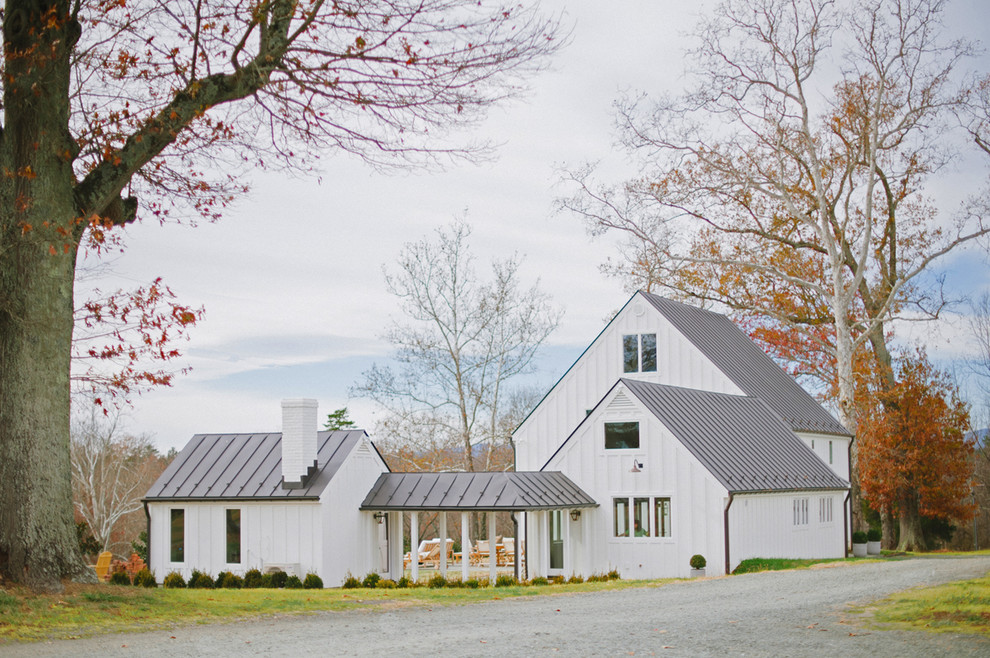 Foto della villa grande bianca country a due piani con rivestimento in metallo, tetto a capanna e copertura in metallo o lamiera