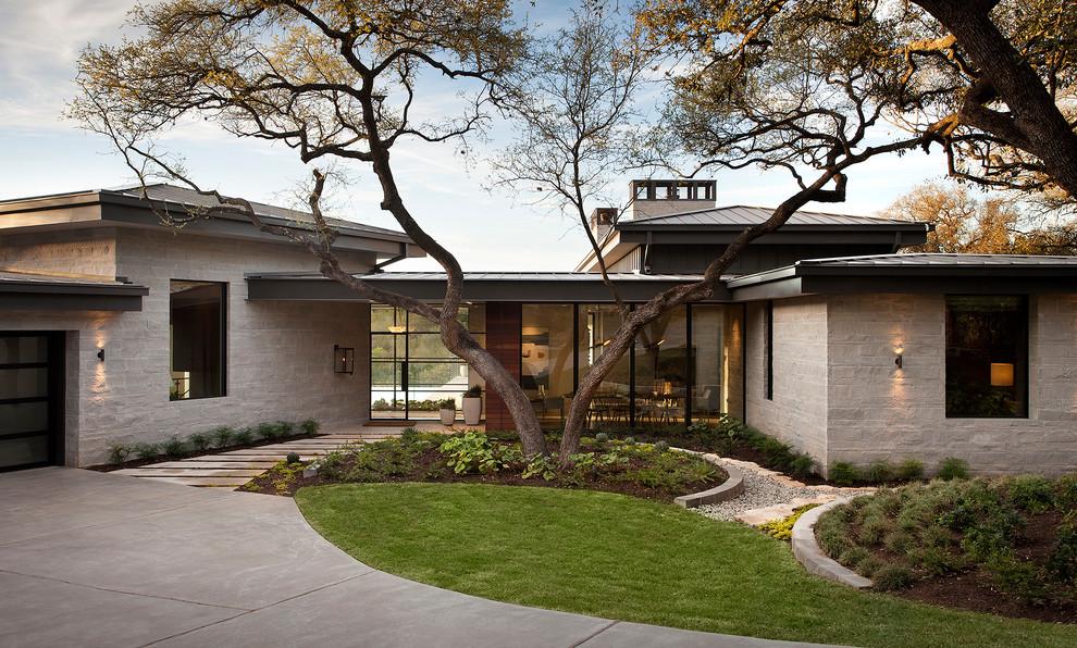 Ejemplo de fachada de casa beige minimalista grande a niveles con revestimiento de piedra, tejado de un solo tendido y tejado de metal