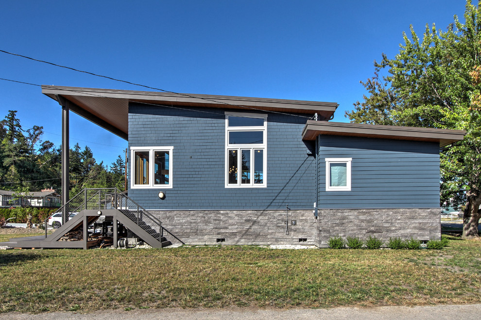 Cette photo montre une petite façade de maison bleue tendance en panneau de béton fibré de plain-pied avec un toit en appentis et un toit en métal.