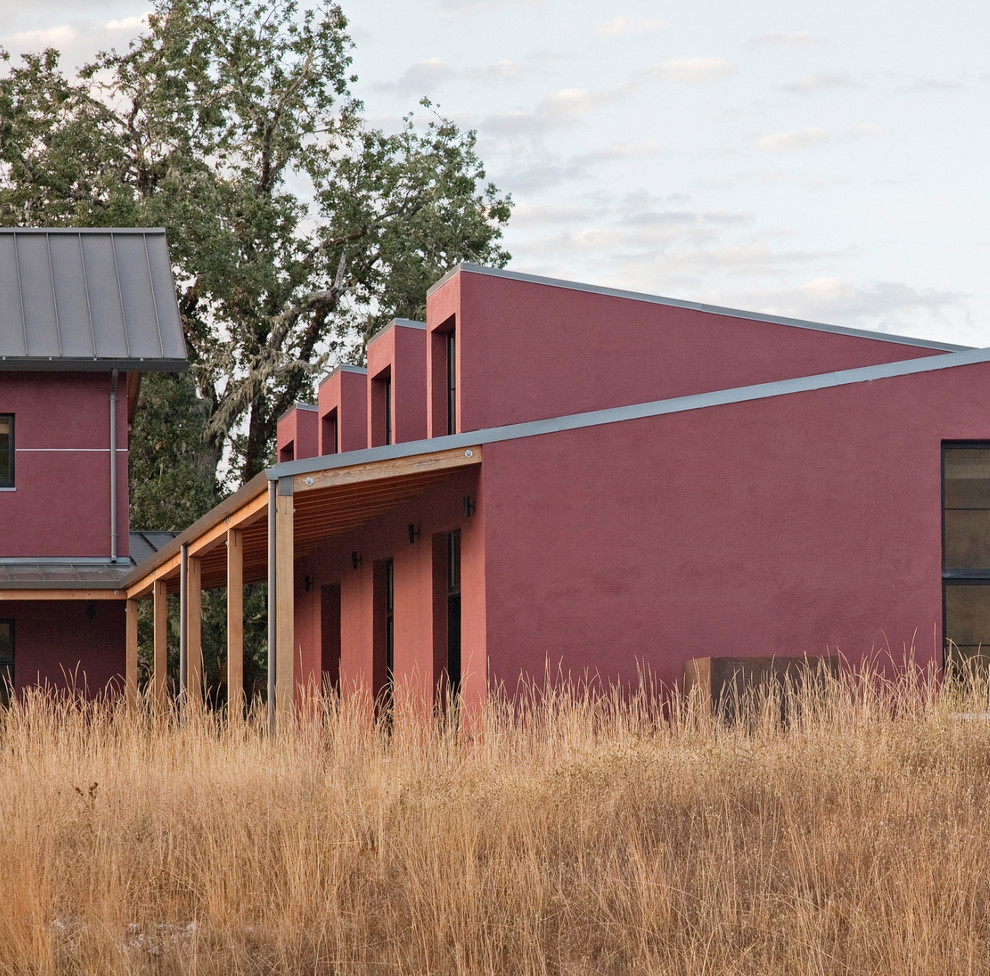 Cette photo montre une grande façade de maison rouge tendance en stuc à un étage avec un toit en métal.