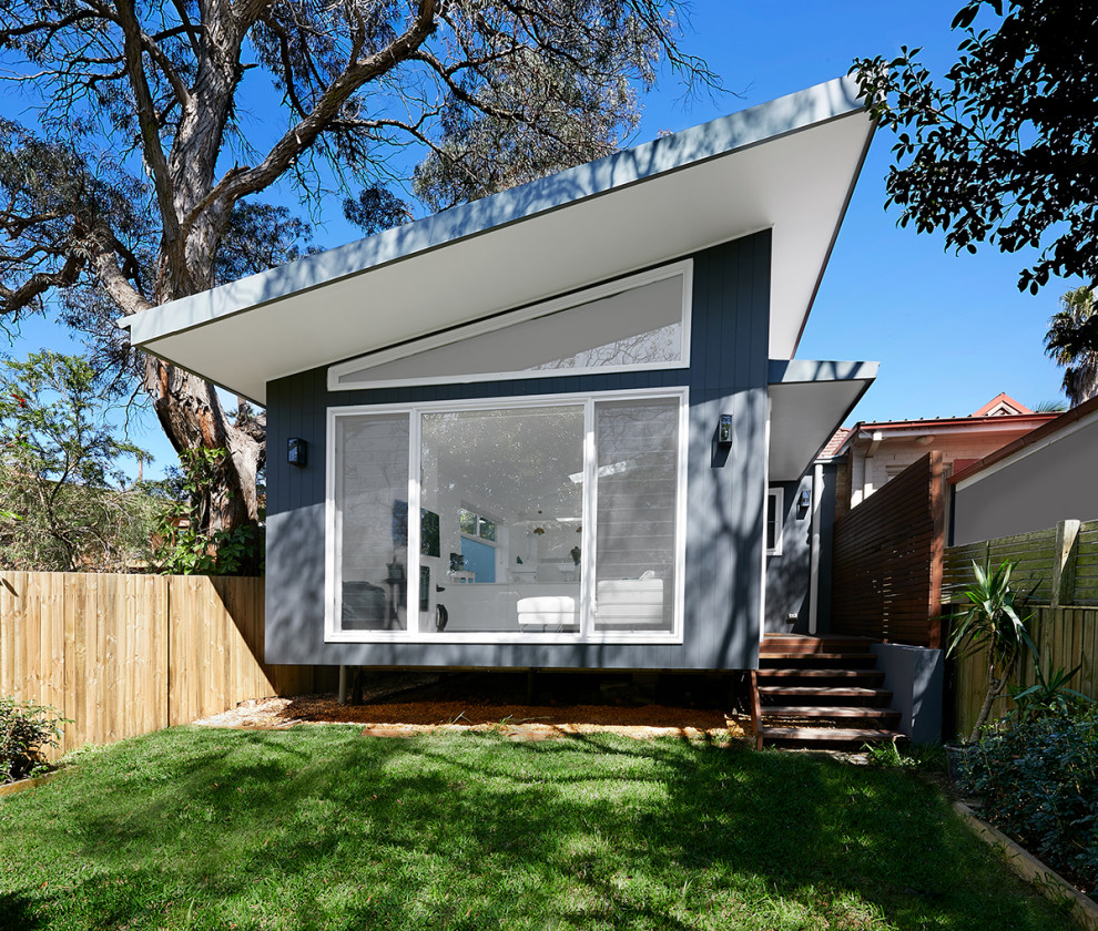 На фото: маленький, одноэтажный, серый частный загородный дом в современном стиле с облицовкой из ЦСП и металлической крышей для на участке и в саду