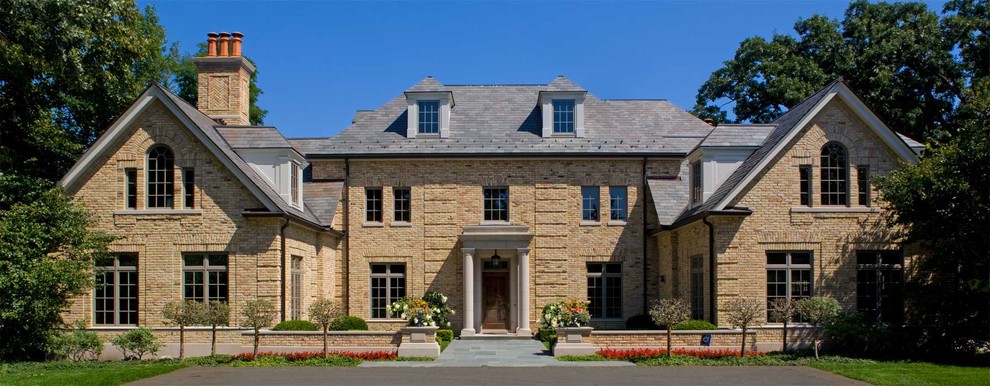 Foto della facciata di una casa grande beige classica a due piani con rivestimento in mattoni e tetto a padiglione