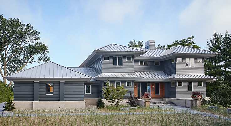 Idée de décoration pour une grande façade de maison grise et métallique design à deux étages et plus avec un toit à quatre pans et un toit en métal.