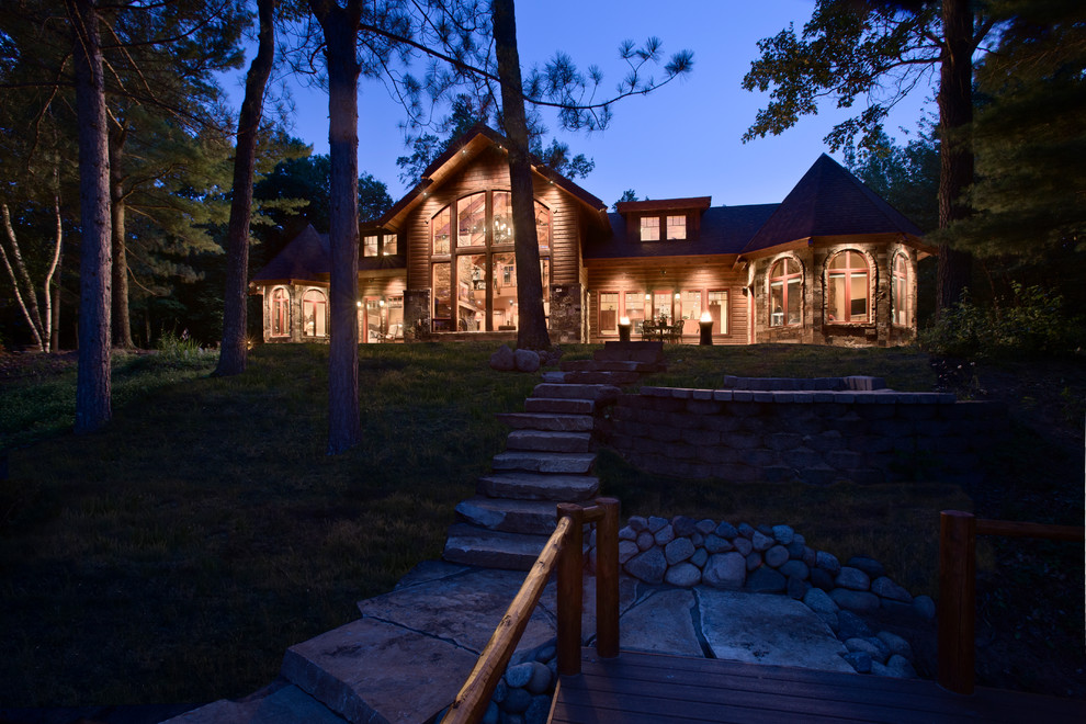 Пример оригинального дизайна: двухэтажный, деревянный, коричневый, большой частный загородный дом в стиле рустика с двускатной крышей и крышей из гибкой черепицы