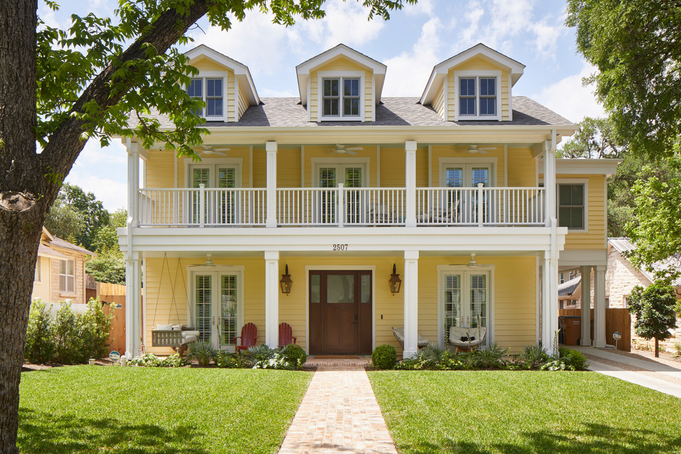 Réalisation d'une grande façade de maison jaune champêtre en bois à un étage avec un toit à deux pans et un toit en shingle.
