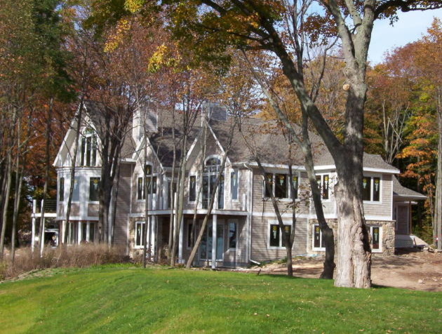 Modelo de fachada gris costera grande de tres plantas con revestimiento de madera y tejado a dos aguas