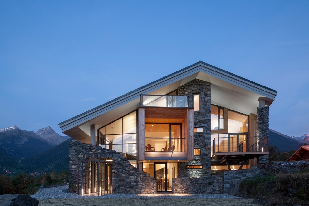 Cette image montre une grande façade de maison grise chalet en pierre à un étage avec un toit à deux pans.