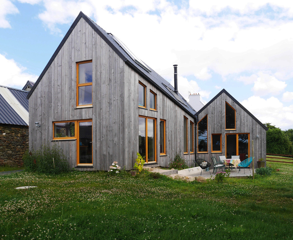 На фото: двухэтажный, деревянный, серый дом в современном стиле с двускатной крышей