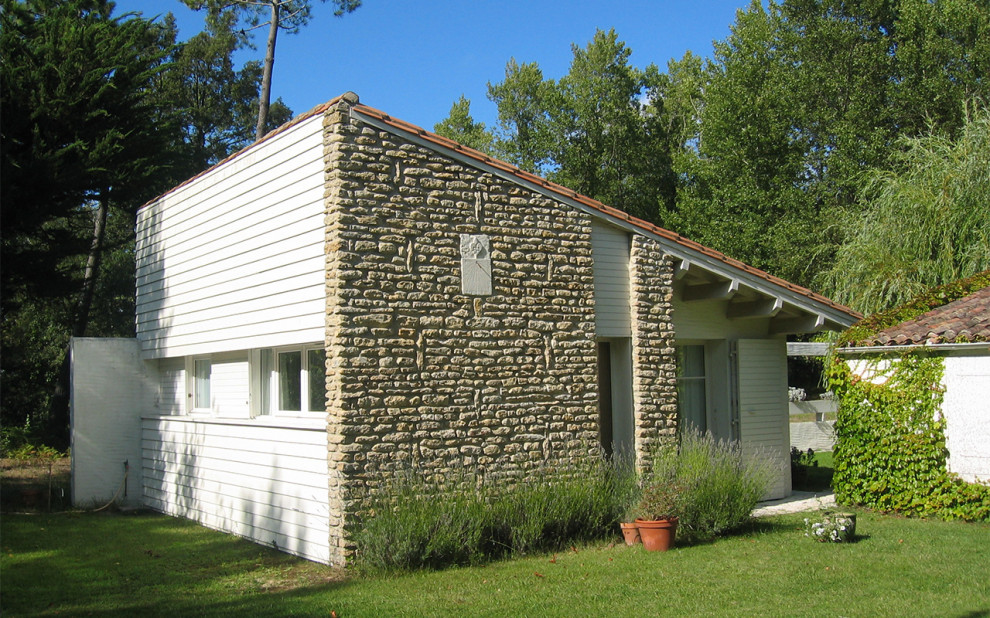 Cette image montre une façade de maison blanche design en pierre de plain-pied avec un toit à deux pans et un toit en tuile.