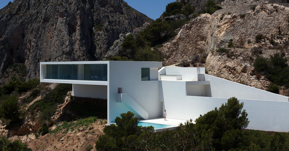 На фото: большой, белый дом в стиле модернизм с разными уровнями, облицовкой из цементной штукатурки и плоской крышей с