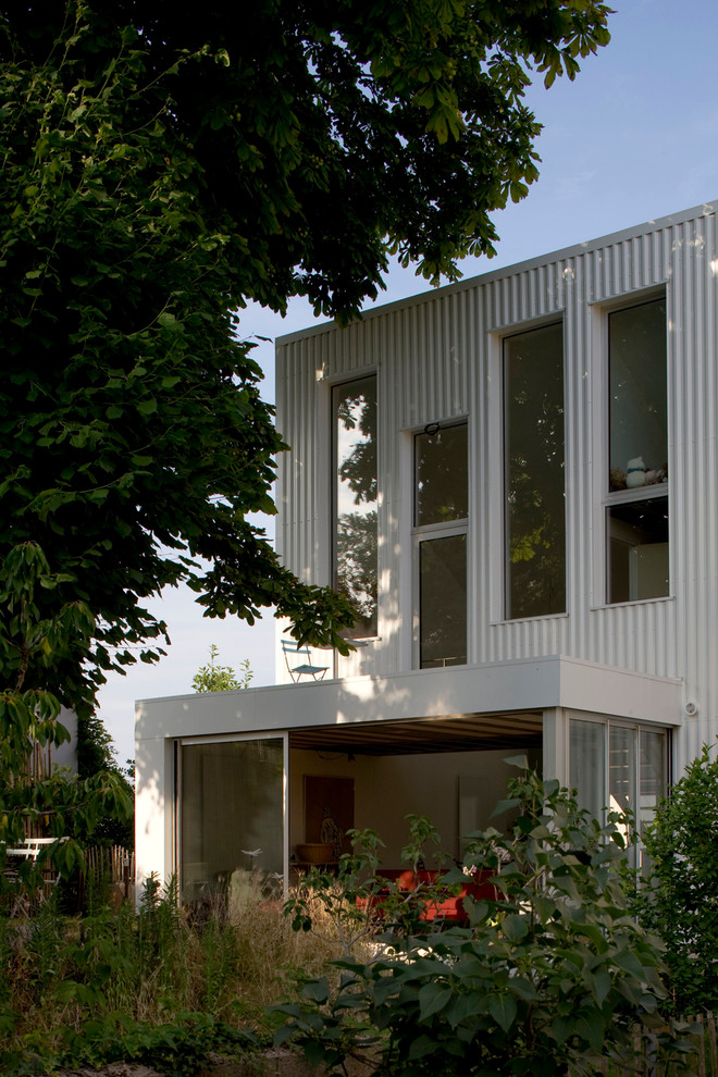 Foto på ett mellanstort funkis vitt hus, med tre eller fler plan, metallfasad och platt tak