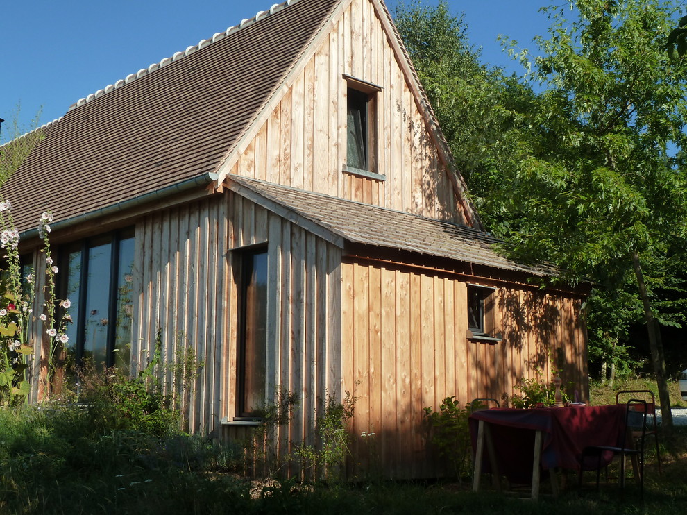 Cette photo montre une façade de maison marron nature en bois de taille moyenne et à un étage avec un toit à deux pans et un toit en tuile.