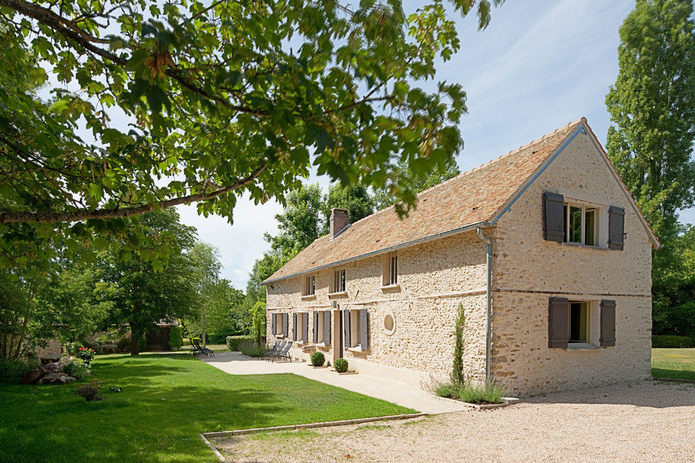 This is an example of a large and beige rural two floor house exterior in Paris with stone cladding and a pitched roof.