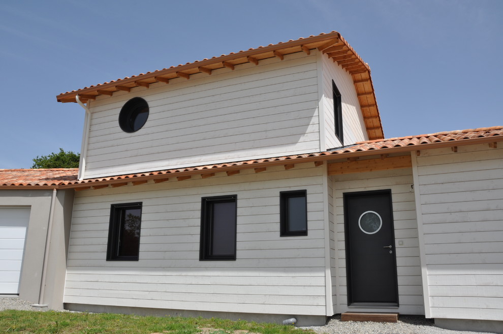 Idée de décoration pour une façade de maison blanche marine en bois de taille moyenne et à un étage avec un toit à quatre pans et un toit en tuile.